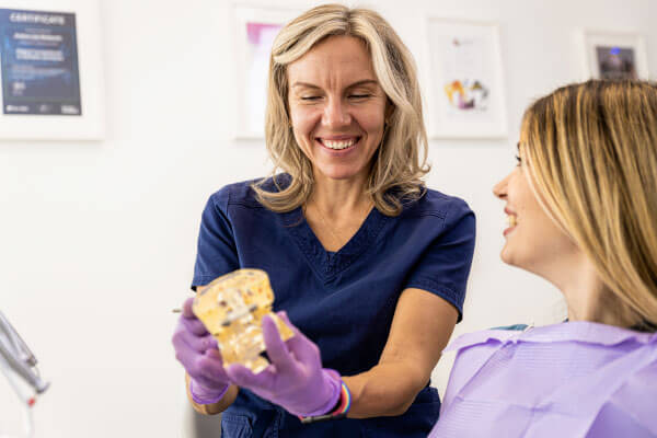 Dentista feminina conversando com paciente mostrando o implante na clínica odontológica